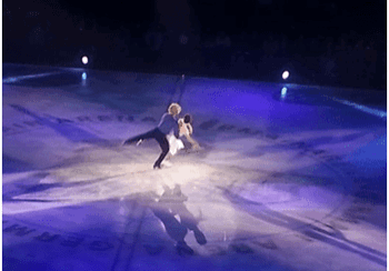 Figure skaters performing a lift on ice under blue lights.